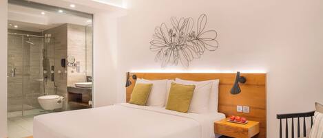 Una habitació d'hotel moderna amb un llit gran, una taula de nit amb una làmpada, una taula petita amb una tassa i una cadira.