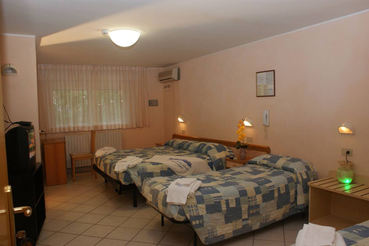 Ein Hotelzimmer mit zwei Betten, einem Schreibtisch, einem Stuhl, einem Heizkörper, einem Fernseher und einem Fenster mit Vorhängen.