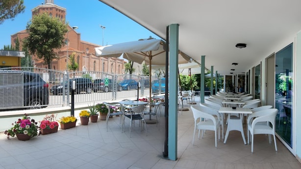 An outdoor patio with white wicker furniture and umbrellas, a tiled floor, and a view of a church tower.