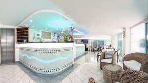 A hotel reception area with a curved counter, a reception desk, a seating area with wicker furniture, and a large window providing a view of the outdoors.