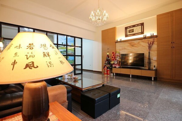 A modern living room with a glass coffee table, a sofa, a lamp with calligraphy, a TV, and wooden cabinets. - Yi Homestay (Taitung)