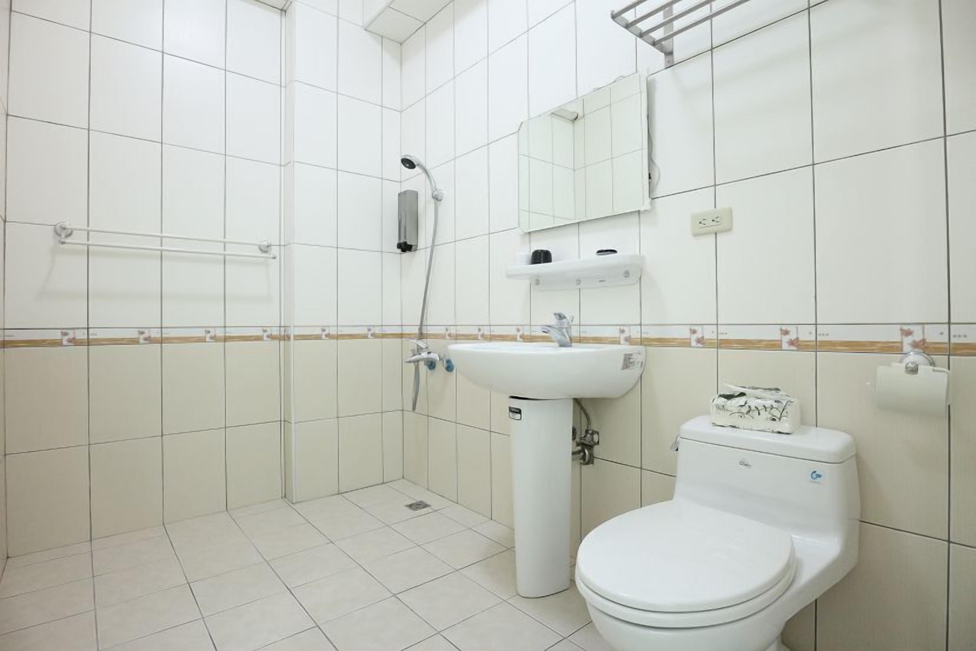 Un baño con azulejos blancos, un lavamanos, un inodoro, una ducha y un espejo.