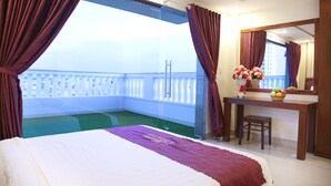 Habitación de hotel con cama, escritorio, silla, espejo y balcón con vistas.