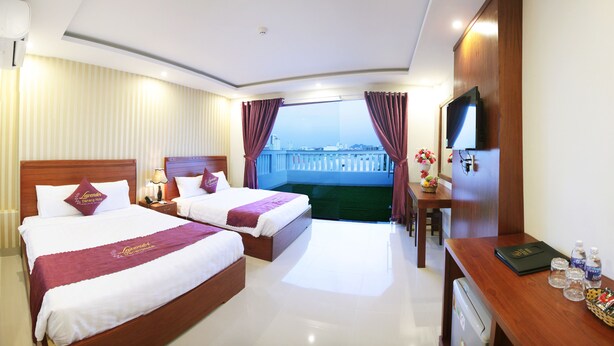Habitación de hotel con dos camas, un escritorio, televisión y balcón con vistas.