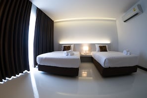 A hotel room with two beds, a nightstand with a lamp, and an air conditioning unit. - Chaisaeng Villa Hotel (Sing Buri)