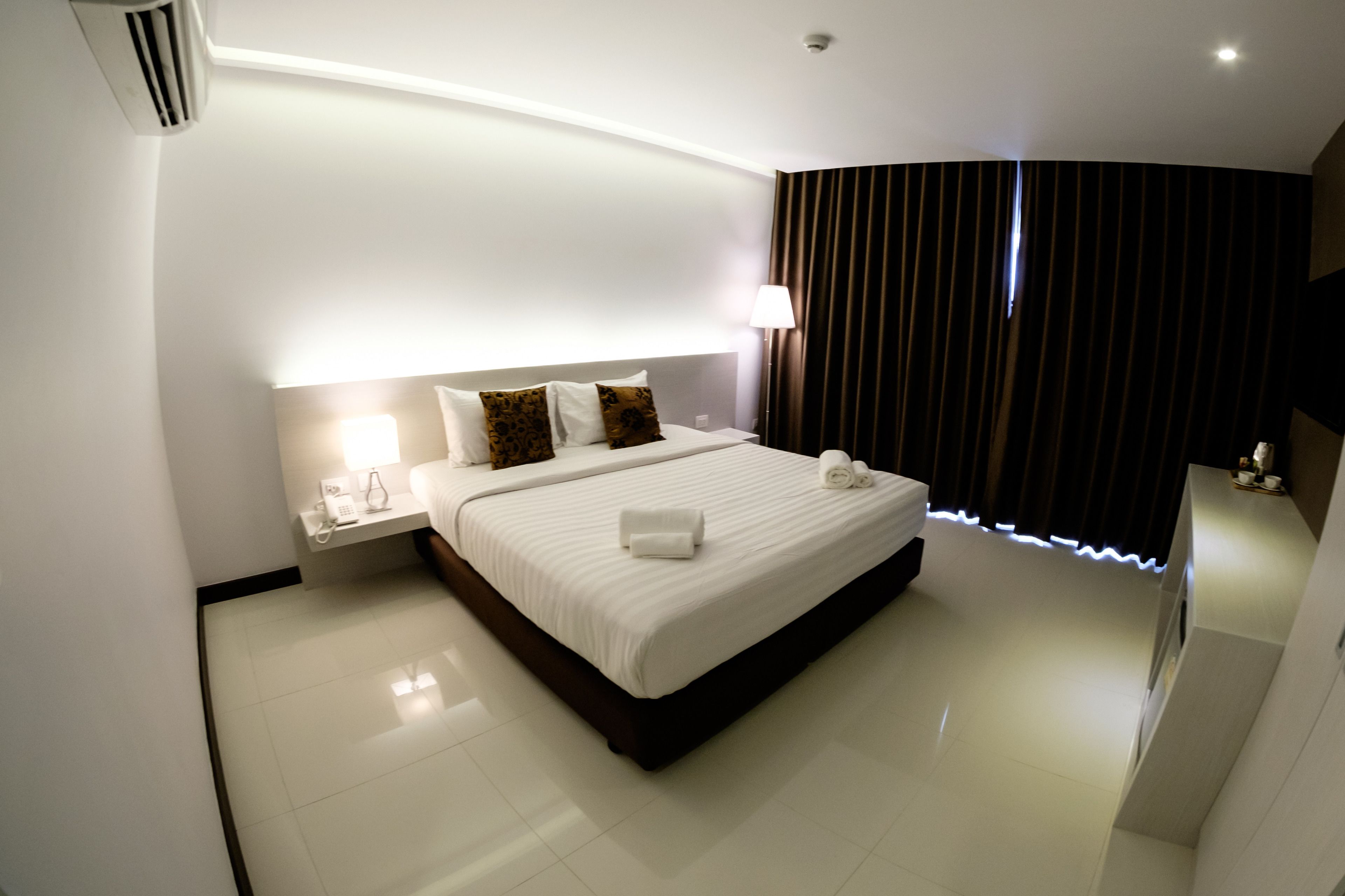Habitación de hotel moderna con una cama grande, una mesita de noche con lámpara y vistas a la ciudad a través de la ventana.