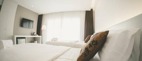 A hotel room with a large bed, a desk with a flat-screen TV, a window with curtains, and a red ceiling light.