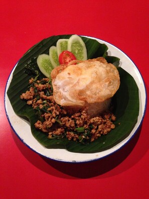 Une assiette de nourriture comprenant un plat frit, de la viande hachée et des légumes, le tout servi sur une feuille de bananier.