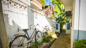 Une ruelle étroite où des vélos sont garés contre un mur blanc, avec un chemin en béton et quelques plantes.