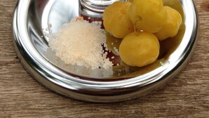 Un verre transparent contenant du thé, une assiette avec des fruits jaunes et une petite pile de granules blancs sur un plateau en métal.