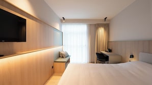 Une chambre d’hôtel avec un lit, un bureau, une chaise, une télévision et une fenêtre avec des rideaux.
