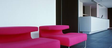 A modern reception area with two bright pink chairs and a white reception desk.