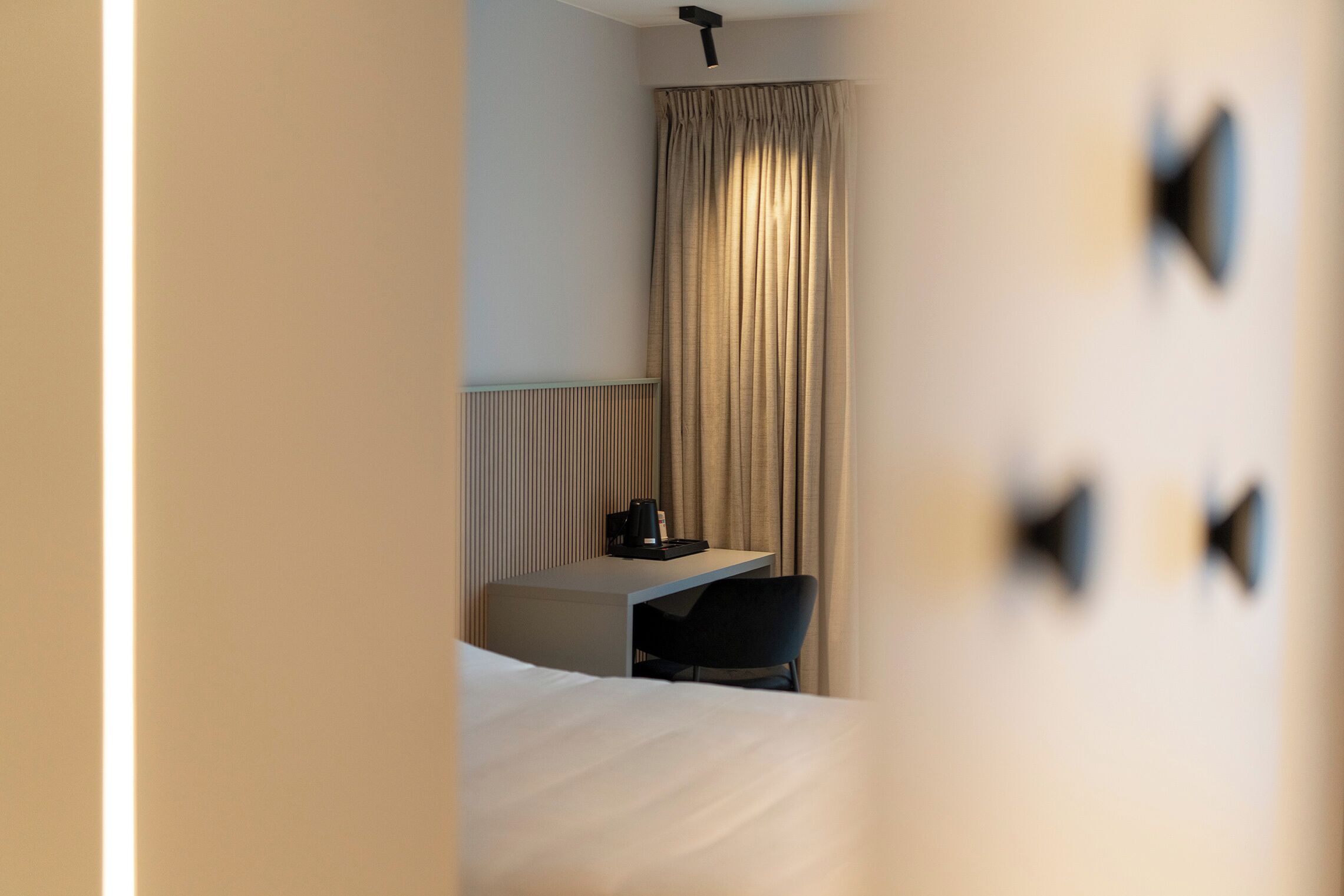 Quarto de hotel com cama, escrivaninha, cadeira e janela com cortinas.