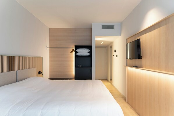 A modern hotel room with a large bed, a built-in wardrobe, a flat-screen TV, and a small seating area with a table and chairs.