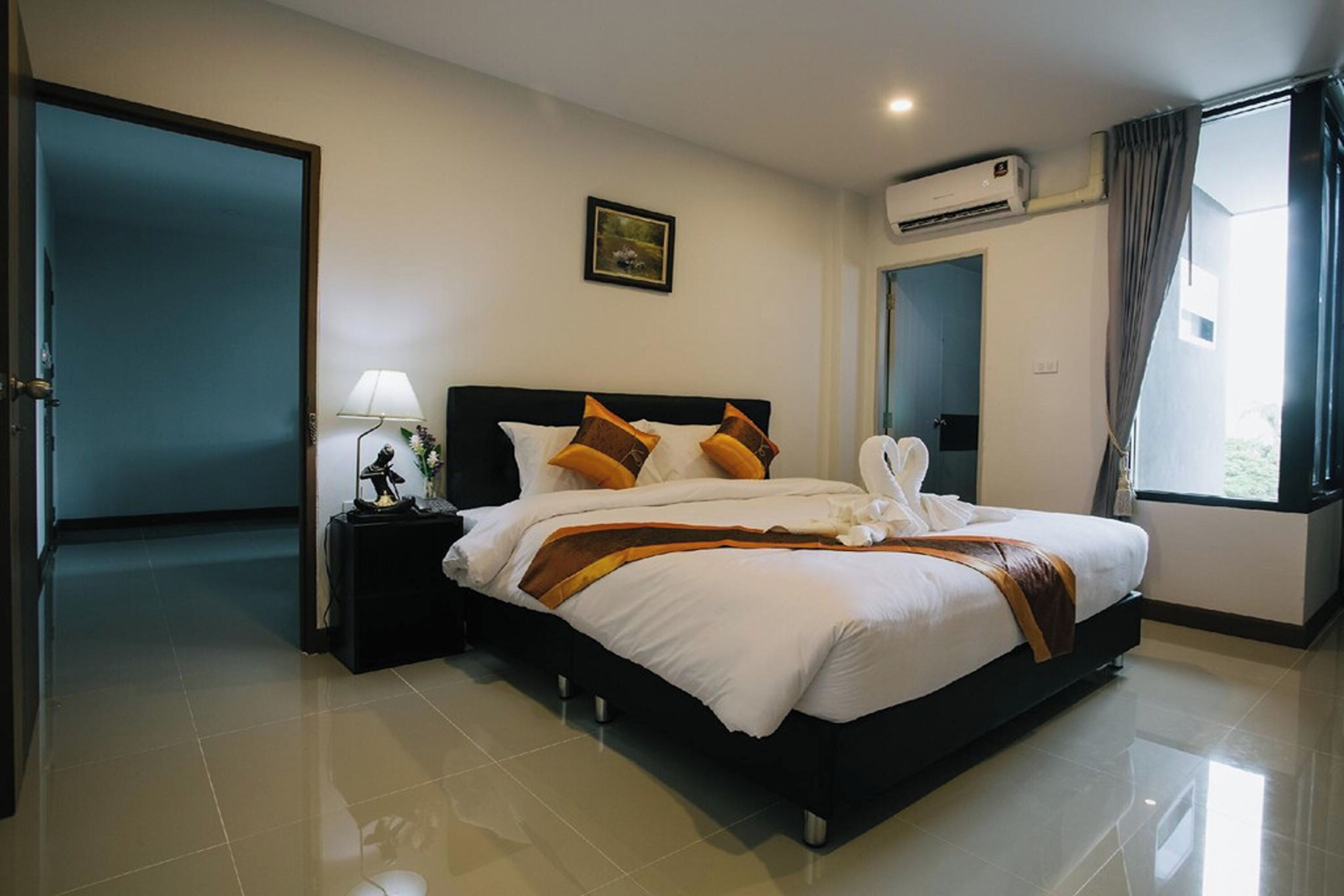 Een hotelkamer met een groot bed, een nachtkastje, een lamp, een foto aan de muur en een airconditioning.