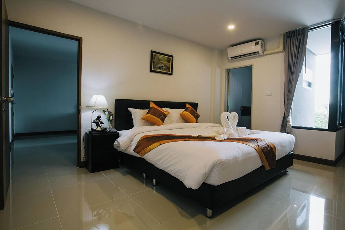 Quarto de hotel com uma cama grande, mesa de cabeceira, abajur, quadro na parede e ar condicionado.