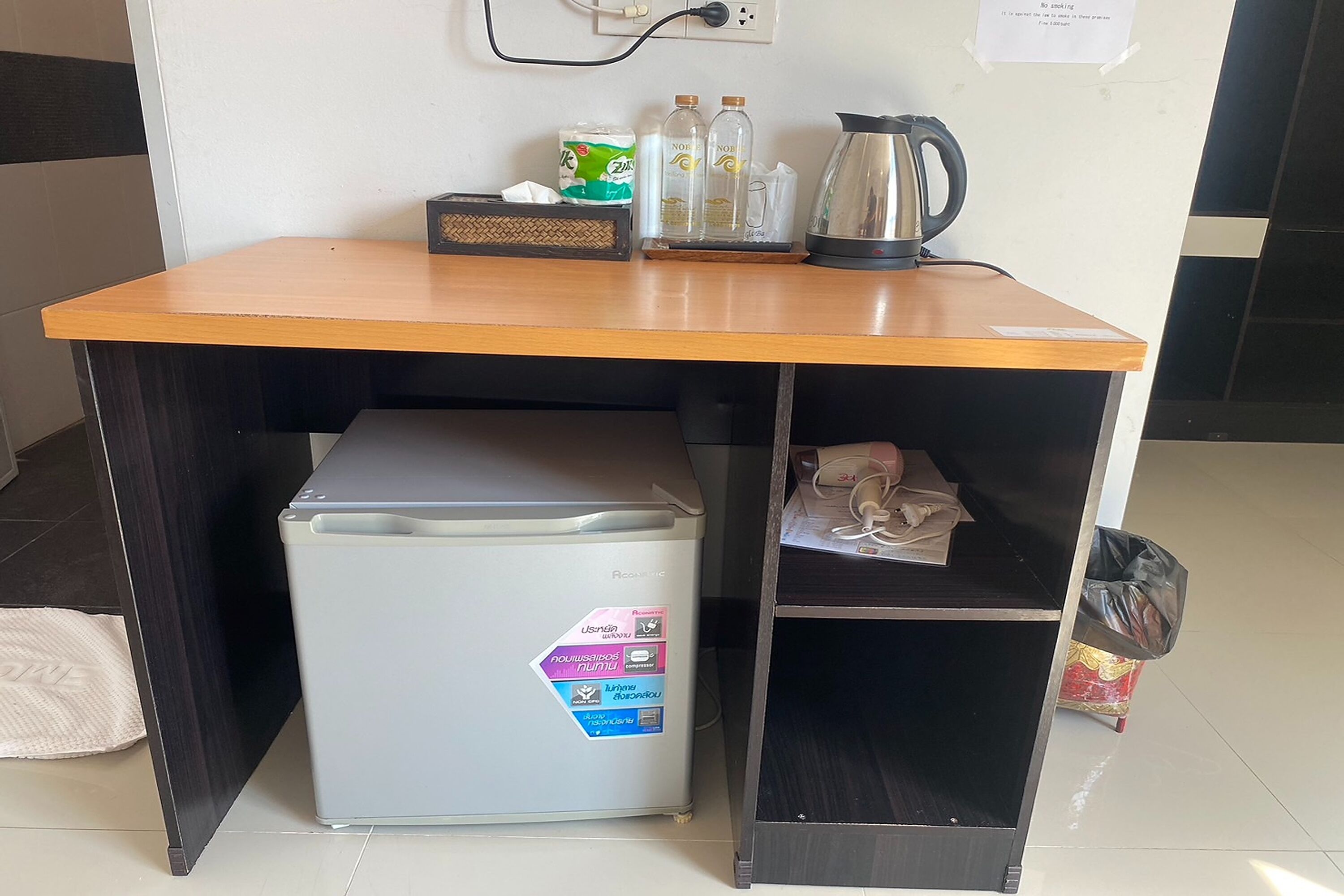 A small kitchenette area with a refrigerator, a coffee maker, and a trash bin.