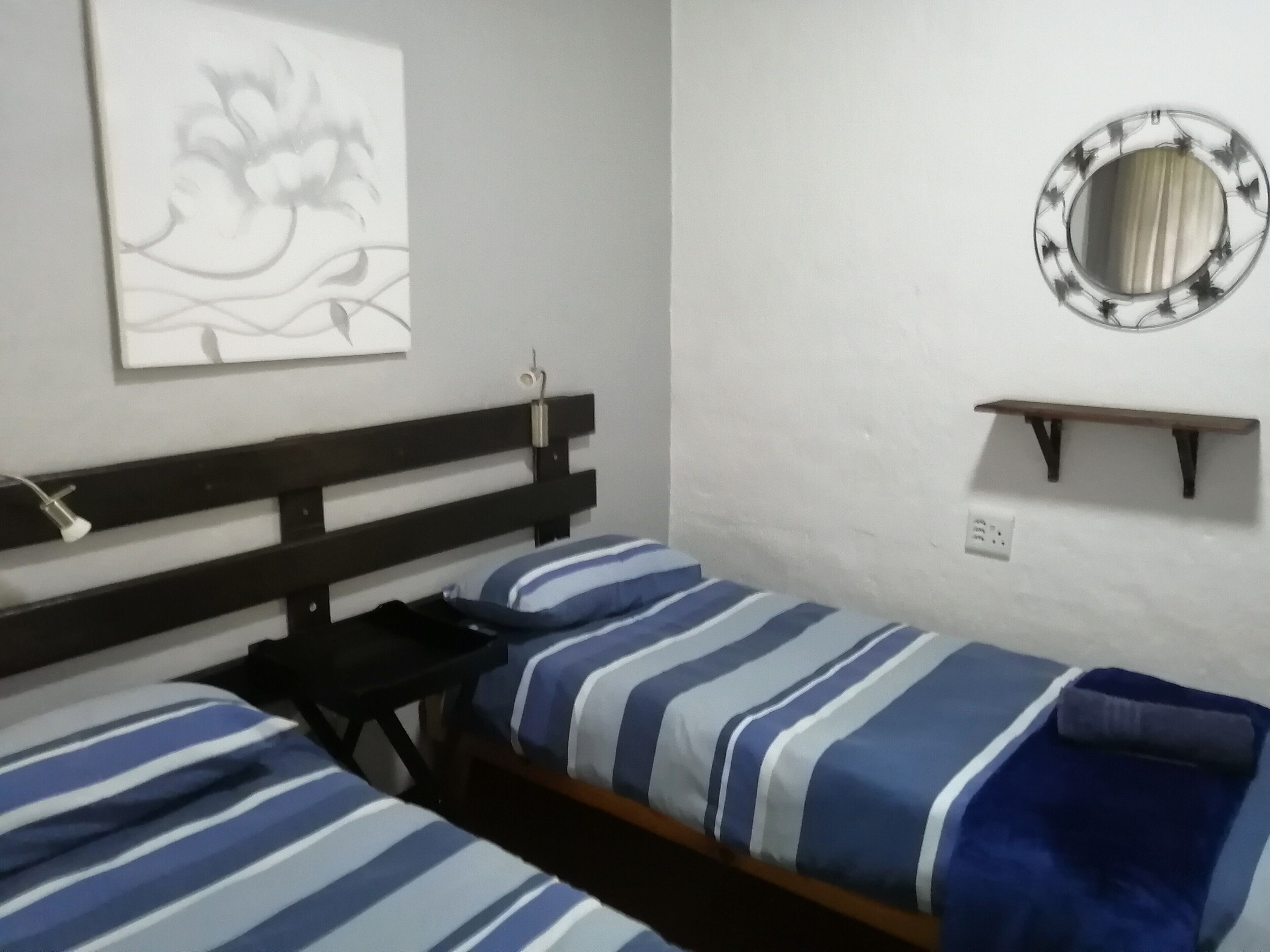 A room with two beds, a wall-mounted mirror, and a small shelf.