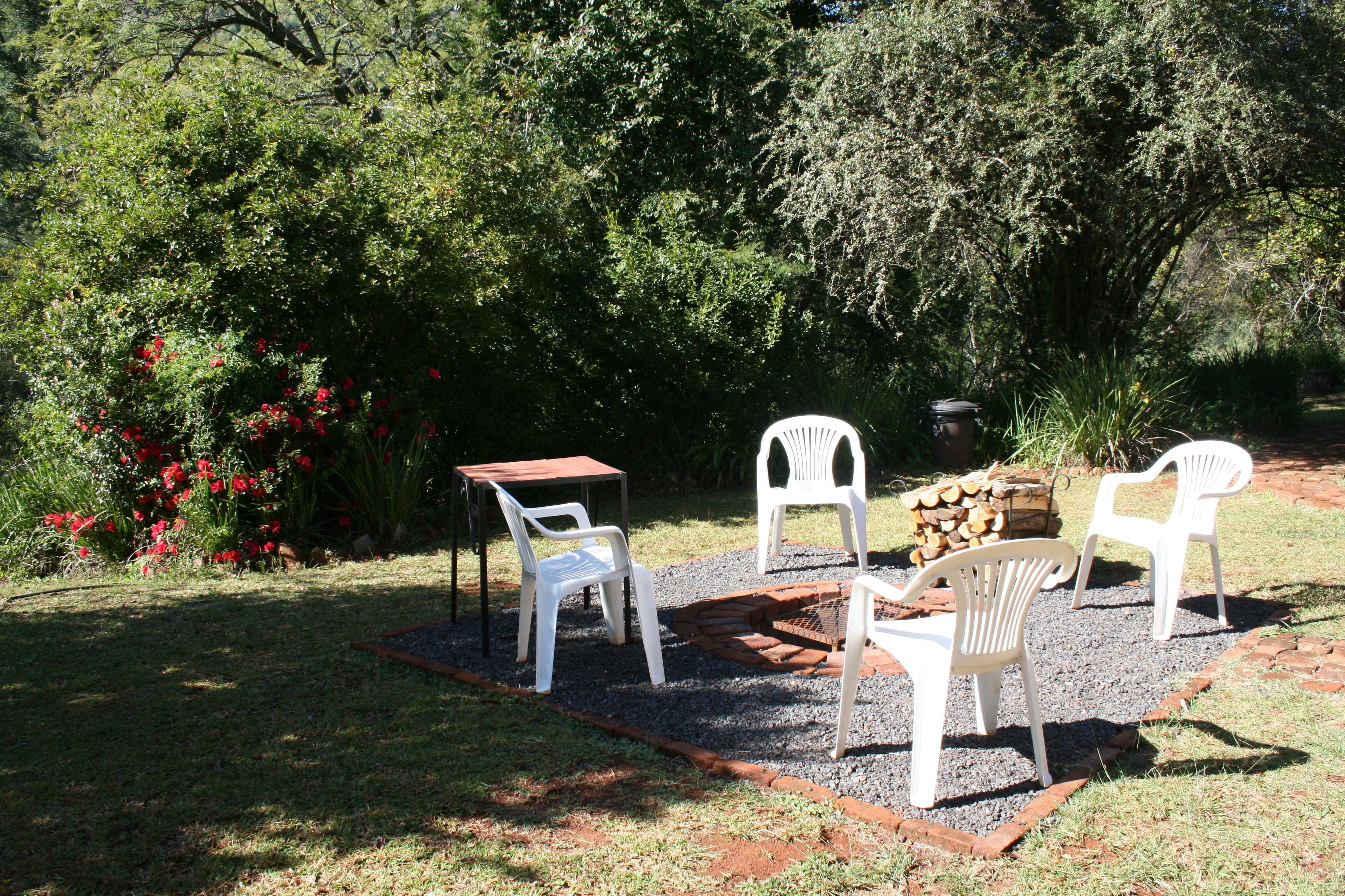 Un espace extérieur aménagé avec une table et quatre chaises blanches, entouré d’un chemin de gravier et de verdure.