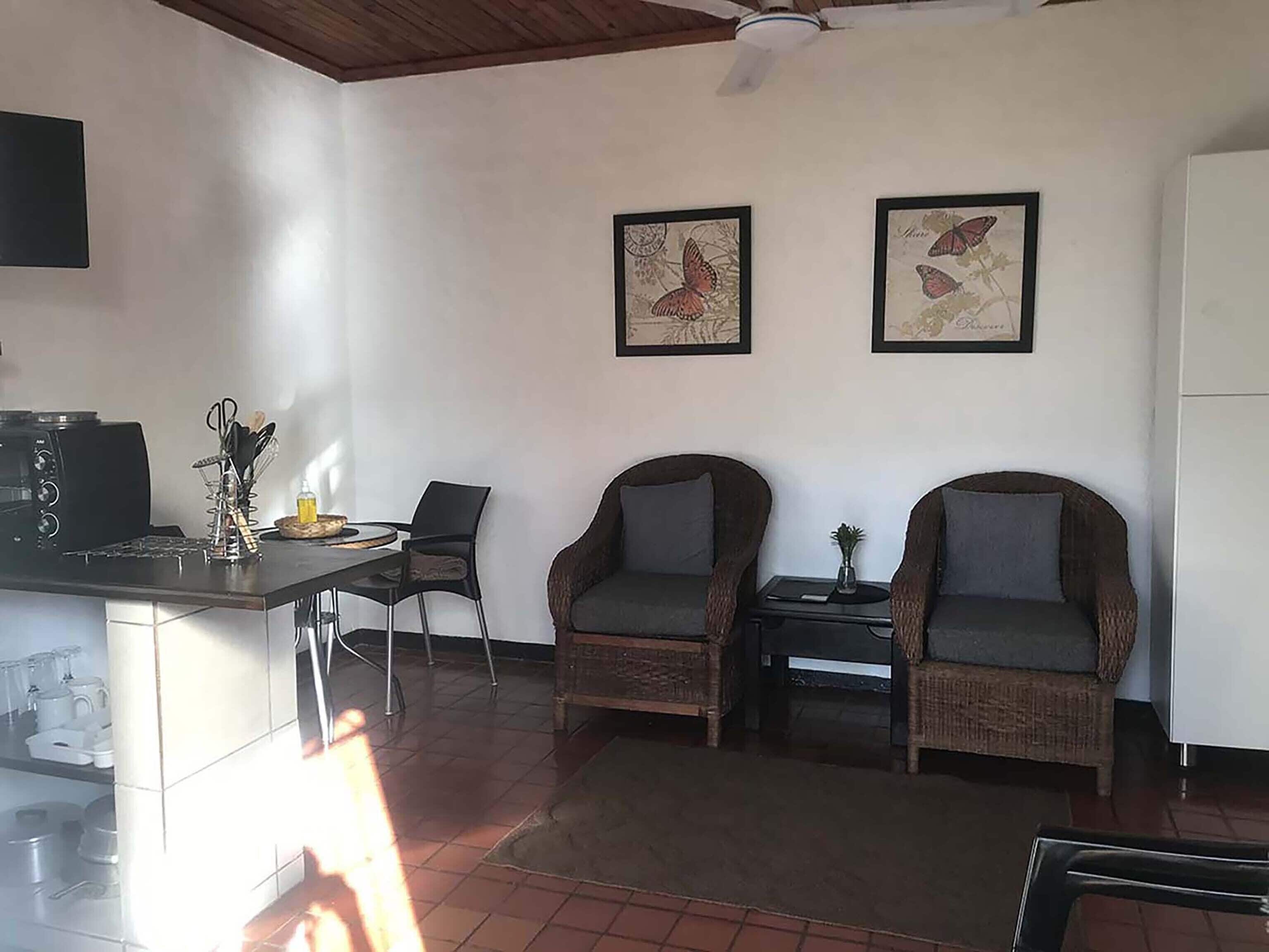 A kitchen with a dining area, two wicker chairs, a ceiling fan, and two framed butterfly pictures on the wall.