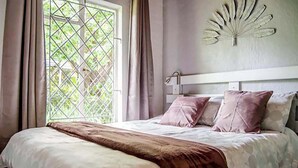 Camera da letto con un letto, tende, una finestra con sbarre di metallo e un ventilatore a parete.