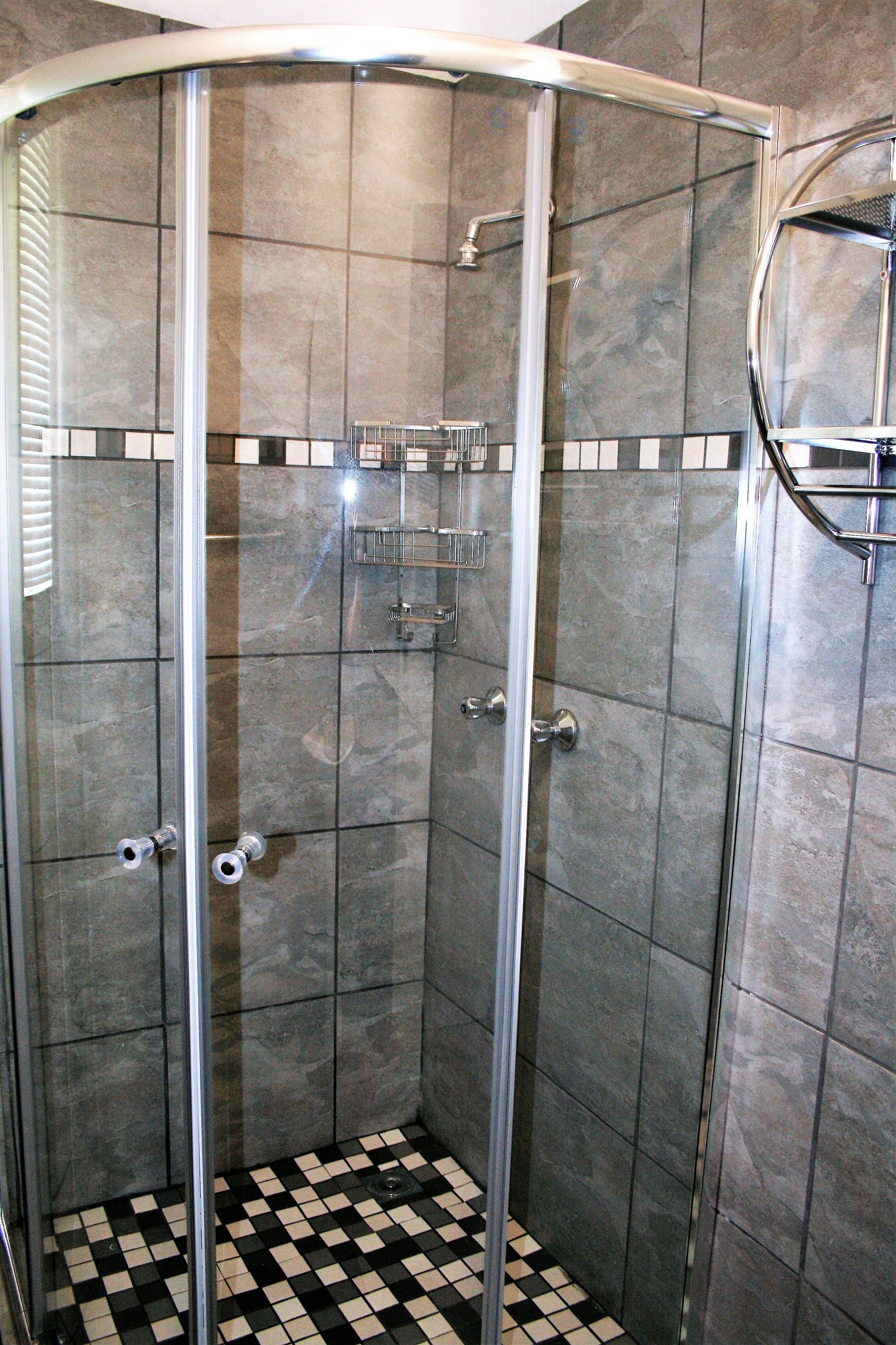 Un vestidor de ducha con paredes de vidrio, suelo a cuadros, un perchero y un espejo en la pared.