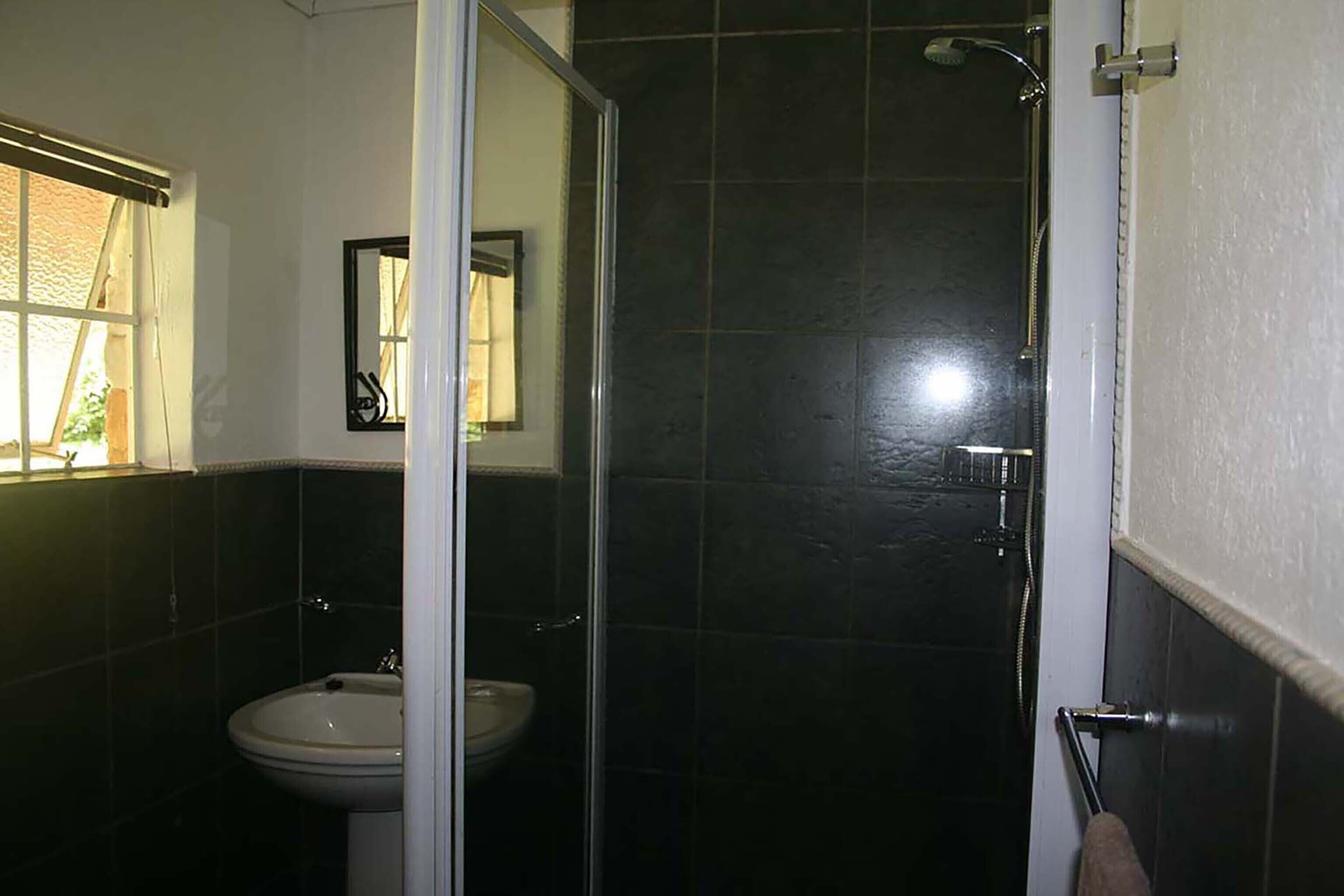 A bathroom with a glass shower enclosure, a sink, and a mirror.