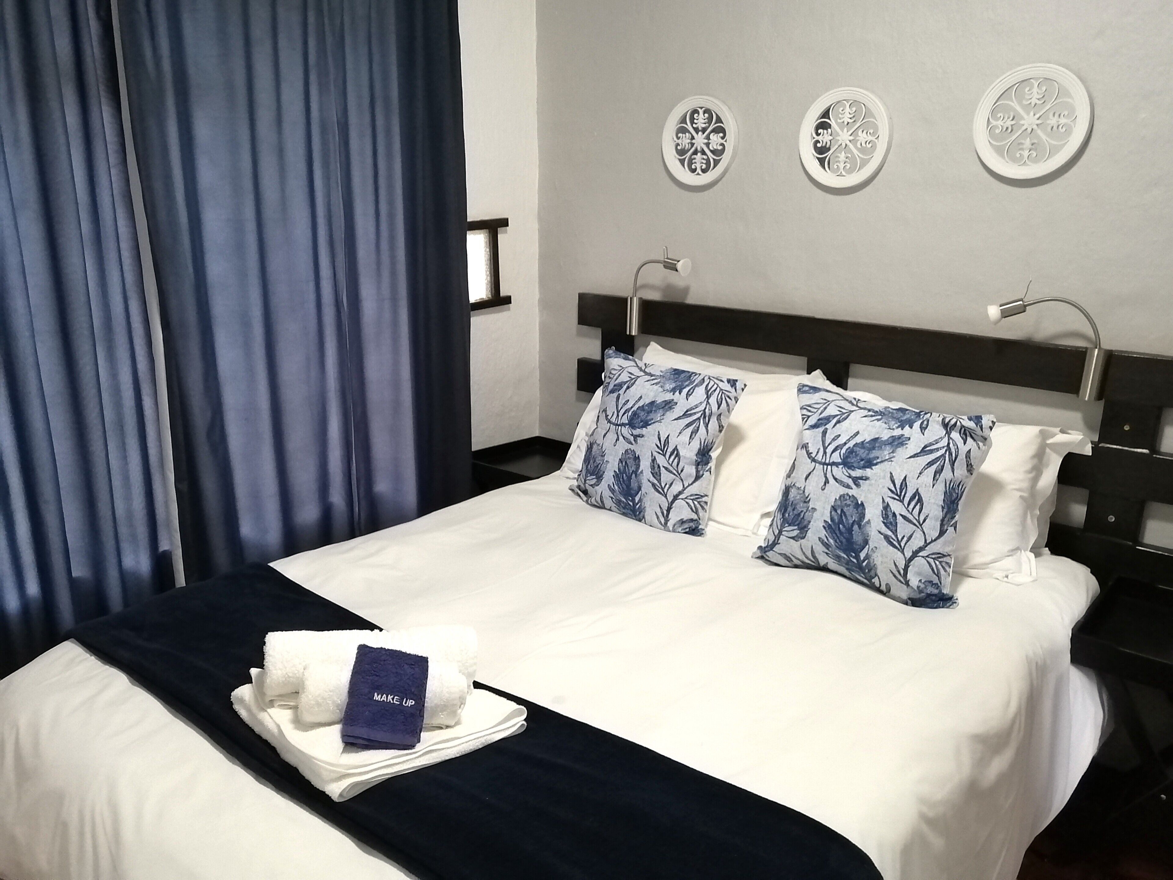 A neatly made bed with white and blue floral pillows, a dark blue bedspread, and a white towel with a blue tag labeled "MAKE UP".
