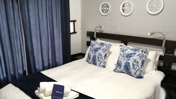A neatly made bed with white and blue floral pillows, a dark blue bedspread, and a white towel with a blue tag labeled "MAKE UP". - Sabi Star Chalets (Sabie)