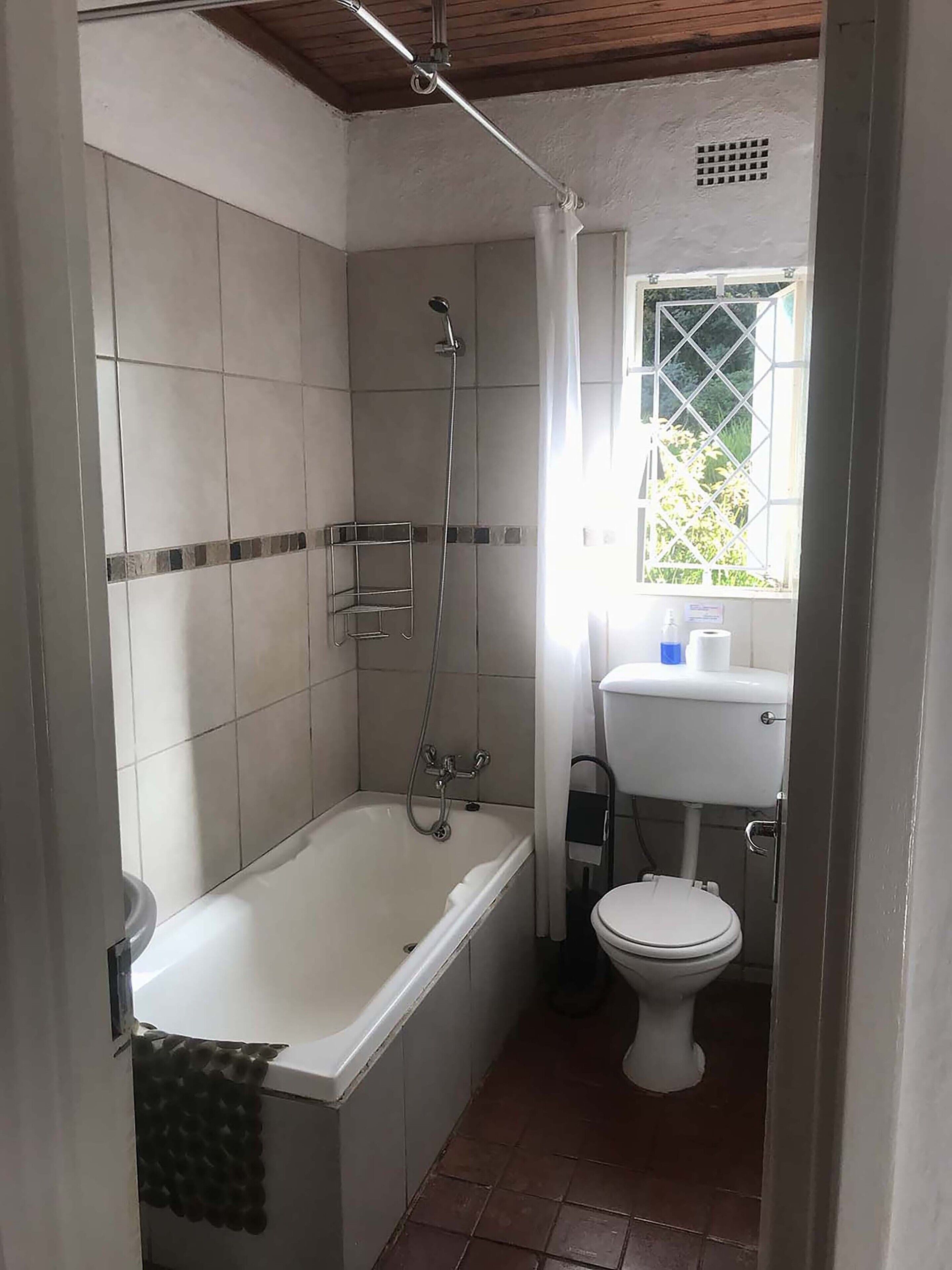 Un baño con bañera, inodoro y ventana con vistas al verdor.