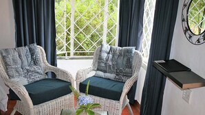 Due sedie in vimini con cuscini decorati, un tavolino con un vaso di fiori e vista attraverso una finestra a griglia.