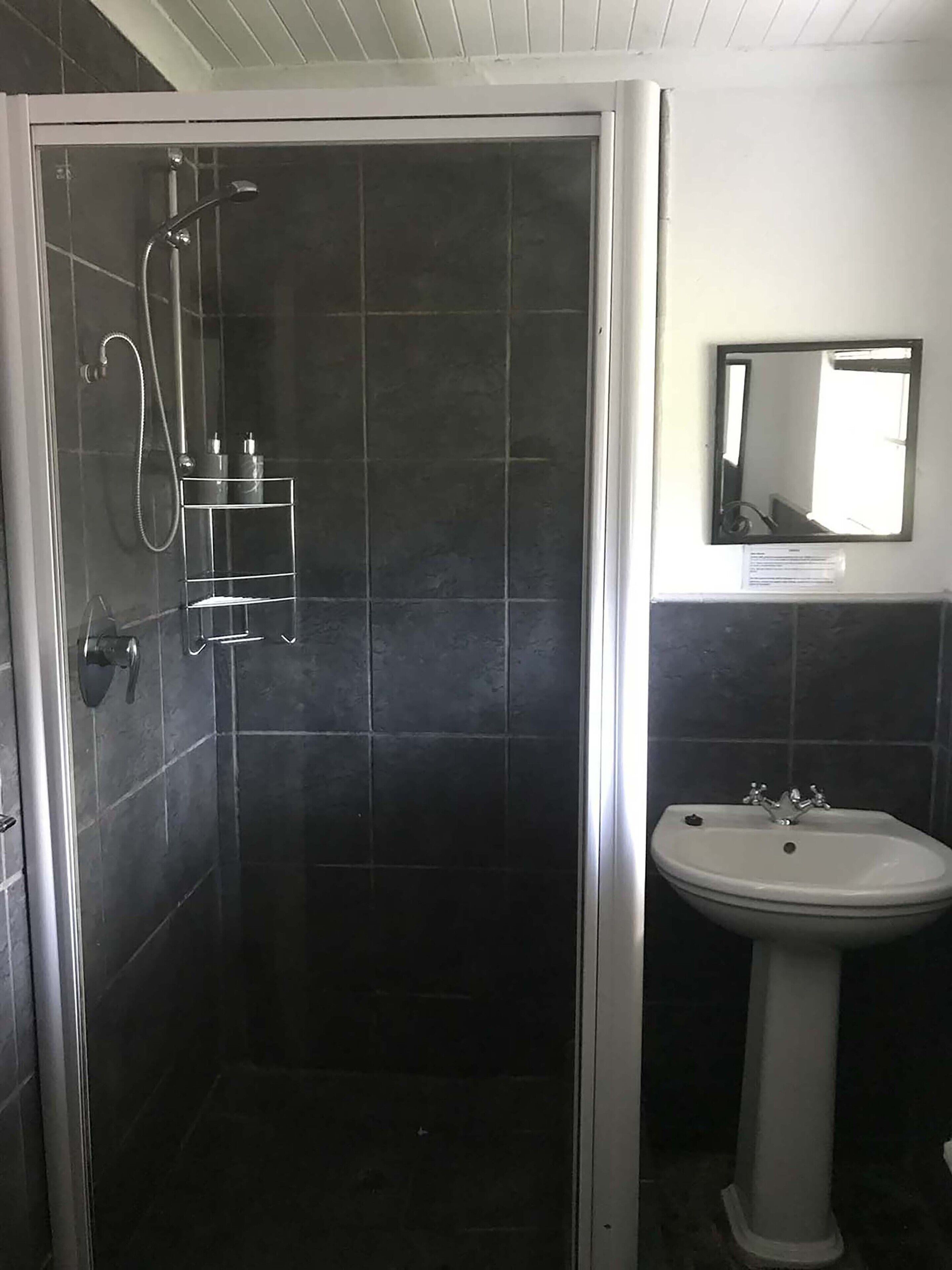 Un baño con ducha de vidrio, lavamanos y espejo.