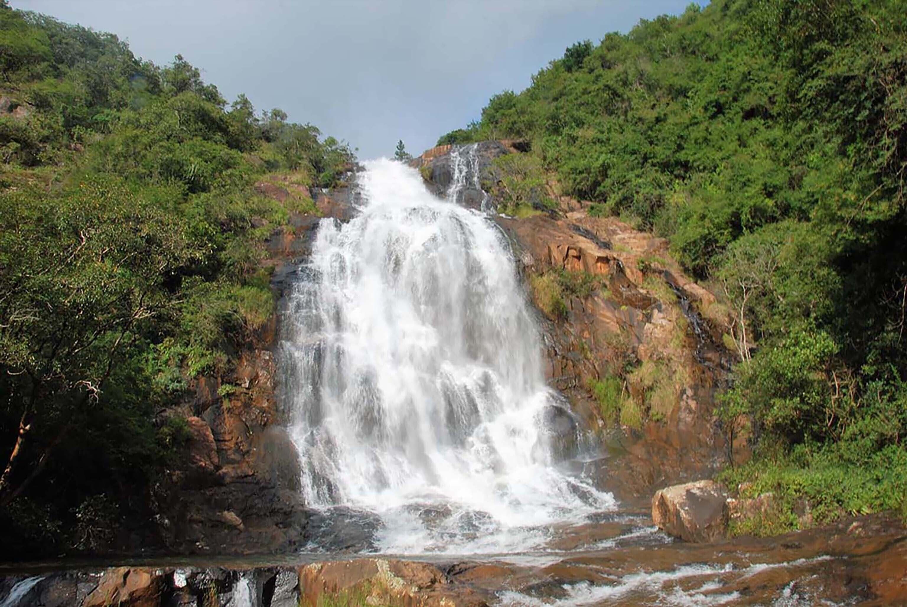 Une cascade se déversant le long d’une falaise rocheuse, entourée d’une végétation luxuriante.