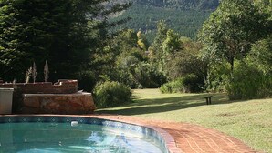 Una piscina con bordo piastrellato, circondata da un patio in mattoni, con sullo sfondo un paesaggio verdeggiante e una montagna.