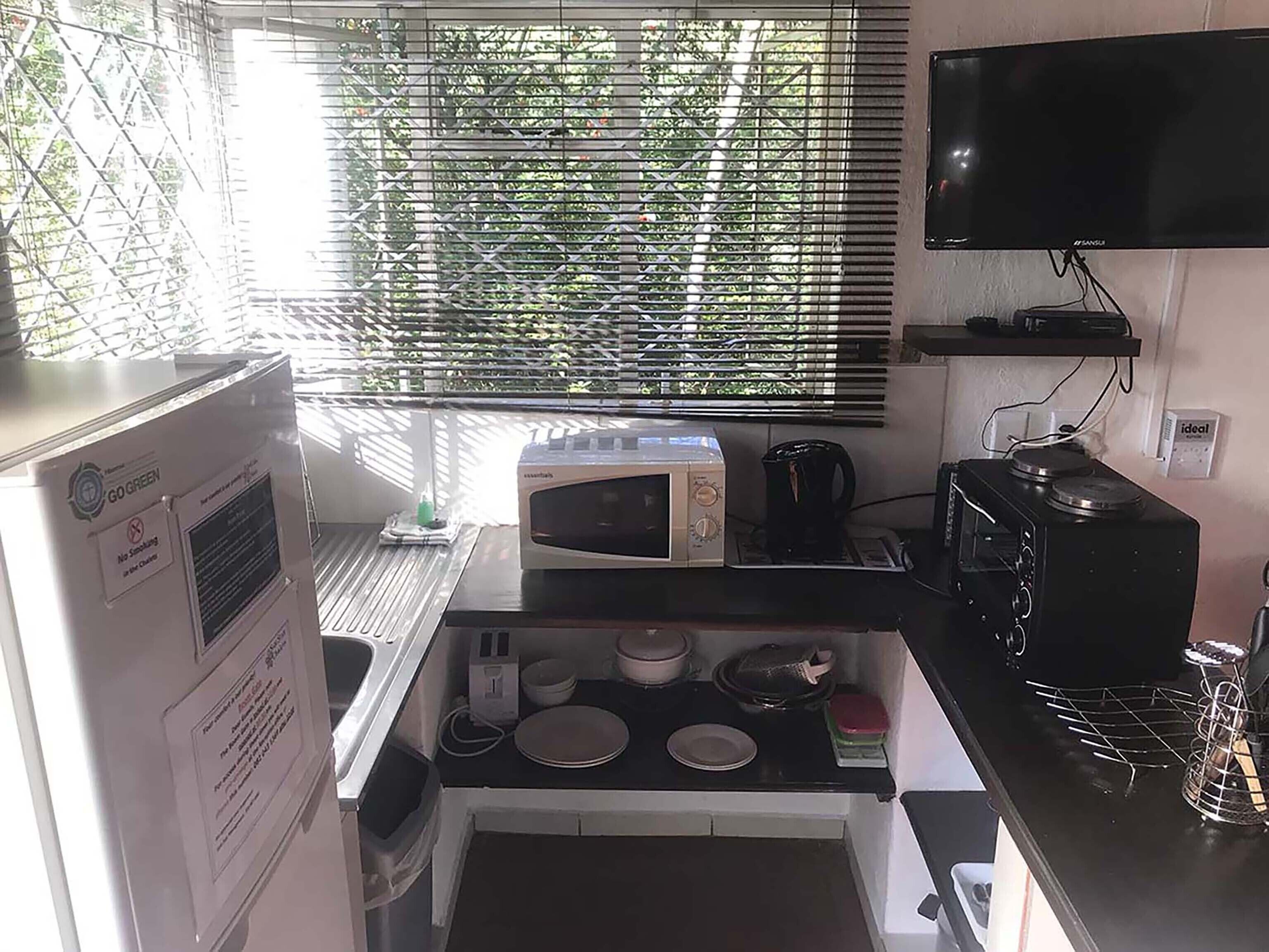 Una cocina compacta equipada con microondas, hervidor y un lavamanos pequeño.