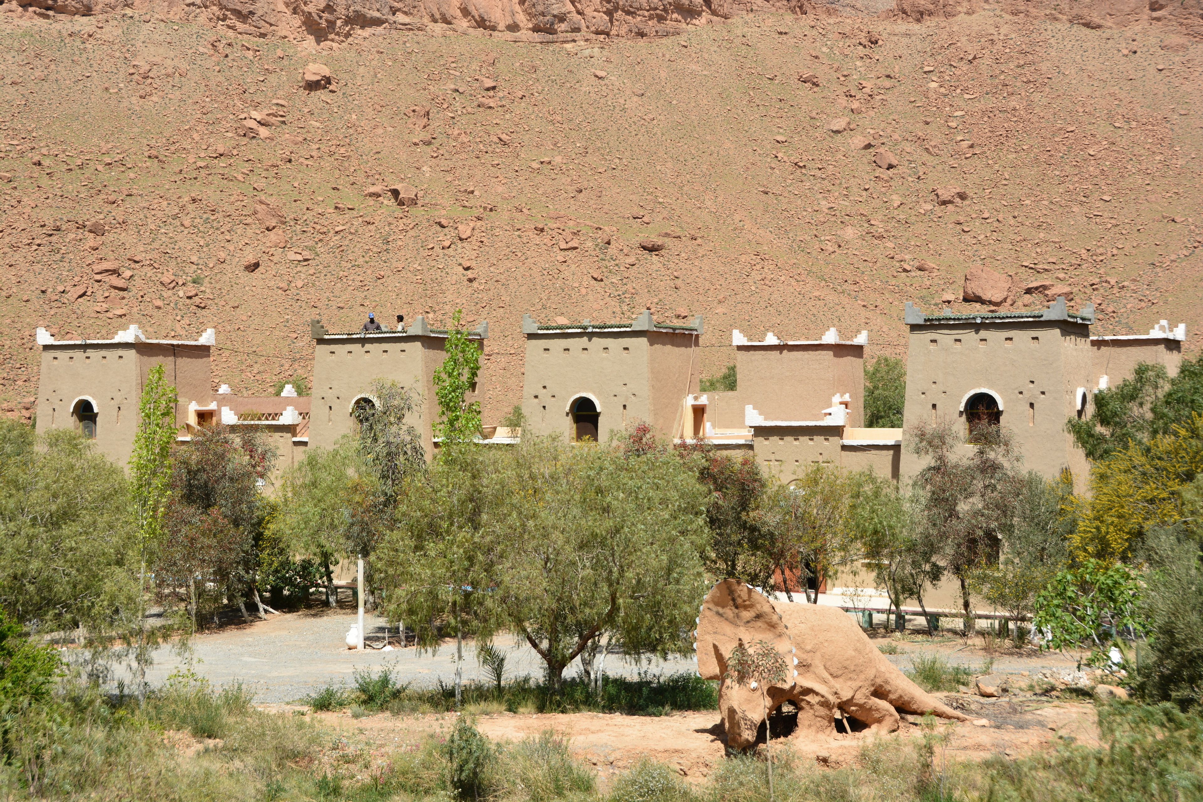 A desert landscape with traditional architecture, including multiple buildings with arched windows and flat roofs, surrounded by sparse vegetation.