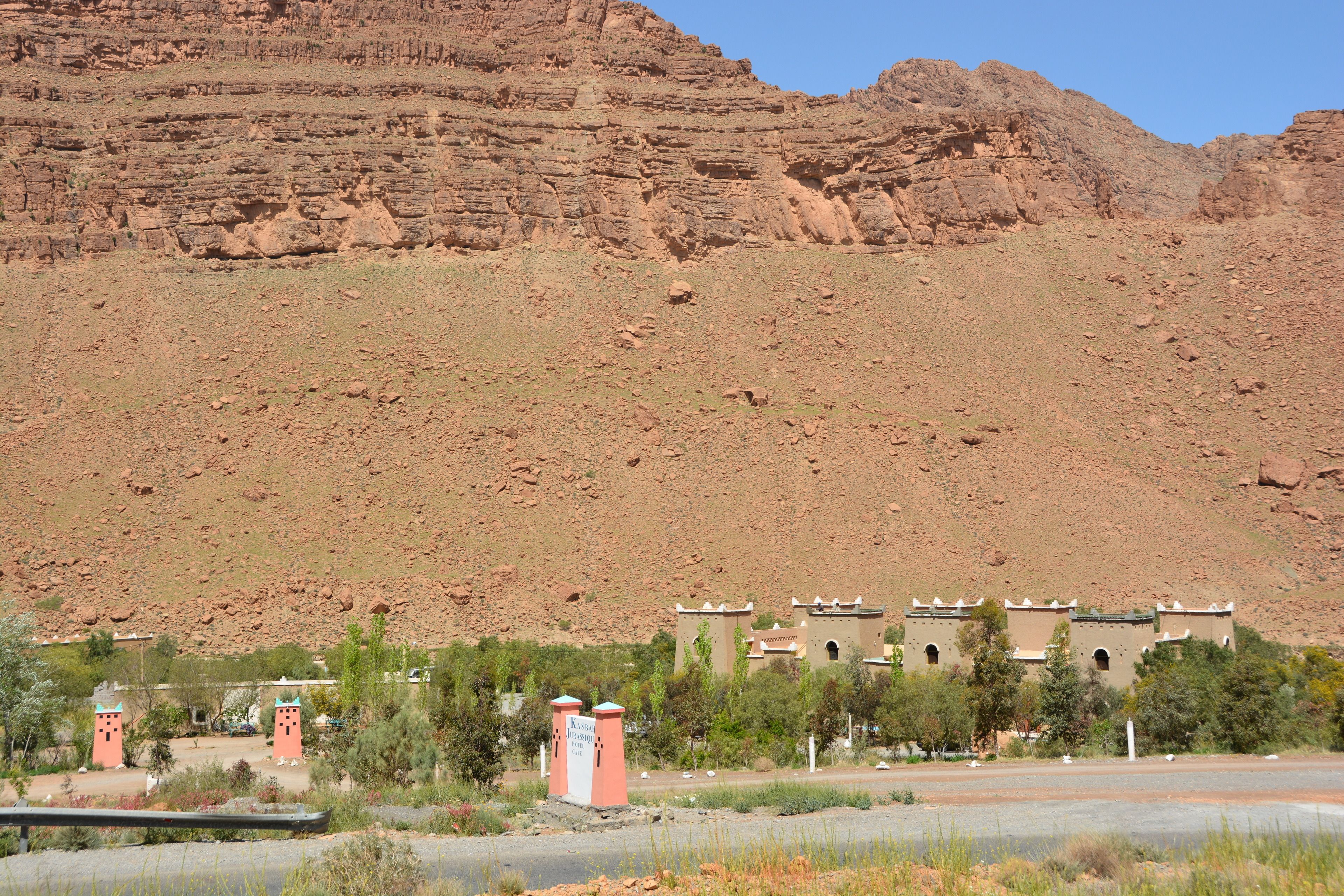 A desert landscape with a building featuring multiple towers and a flat-roofed structure.