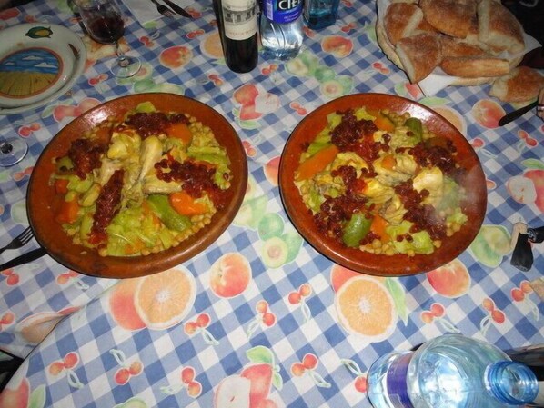 Two large ceramic dishes filled with a stew-like meal, placed on a table with a checkered tablecloth featuring fruit patterns. - Kasbah Hotel Camping Jurassique (Lkheng)