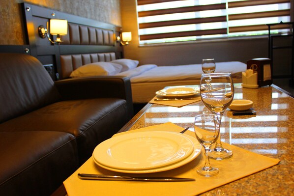 A neatly arranged hotel room with a bed, a leather sofa, a dining area with plates, glasses, and cutlery. - Avan Plaza (Yerevan)