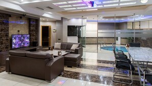 A modern hotel lobby with a seating area, a pool, and a television displaying a sports event. - Avan Plaza (Yerevan)