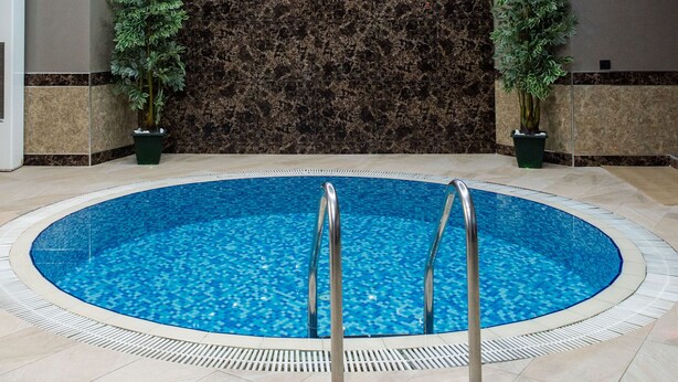 A modern indoor swimming pool with a circular design, surrounded by a tiled floor and a marble wall. - Avan Plaza (Yerevan)