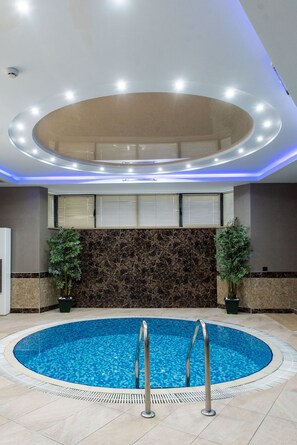 A modern indoor swimming pool with a circular design, surrounded by a tiled floor and a marble wall. - Avan Plaza (Yerevan)