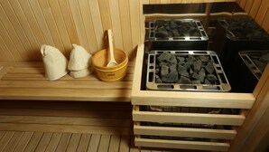 A sauna with wooden benches, a wooden basin with a ladle, and multiple trays of heated stones. - Avan Plaza (Yerevan)