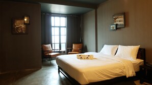 A hotel room with a large bed, two chairs, a small table, and a window with curtains.