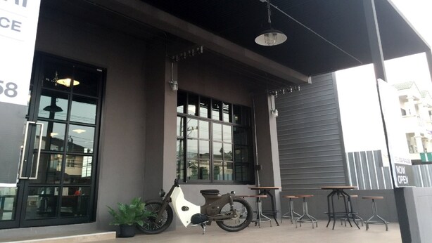 A building with a covered outdoor seating area, a bicycle, and a sign indicating the establishment is now open.
