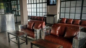 A modern lounge area with leather sofas and metal-framed tables, large windows, and a television screen.