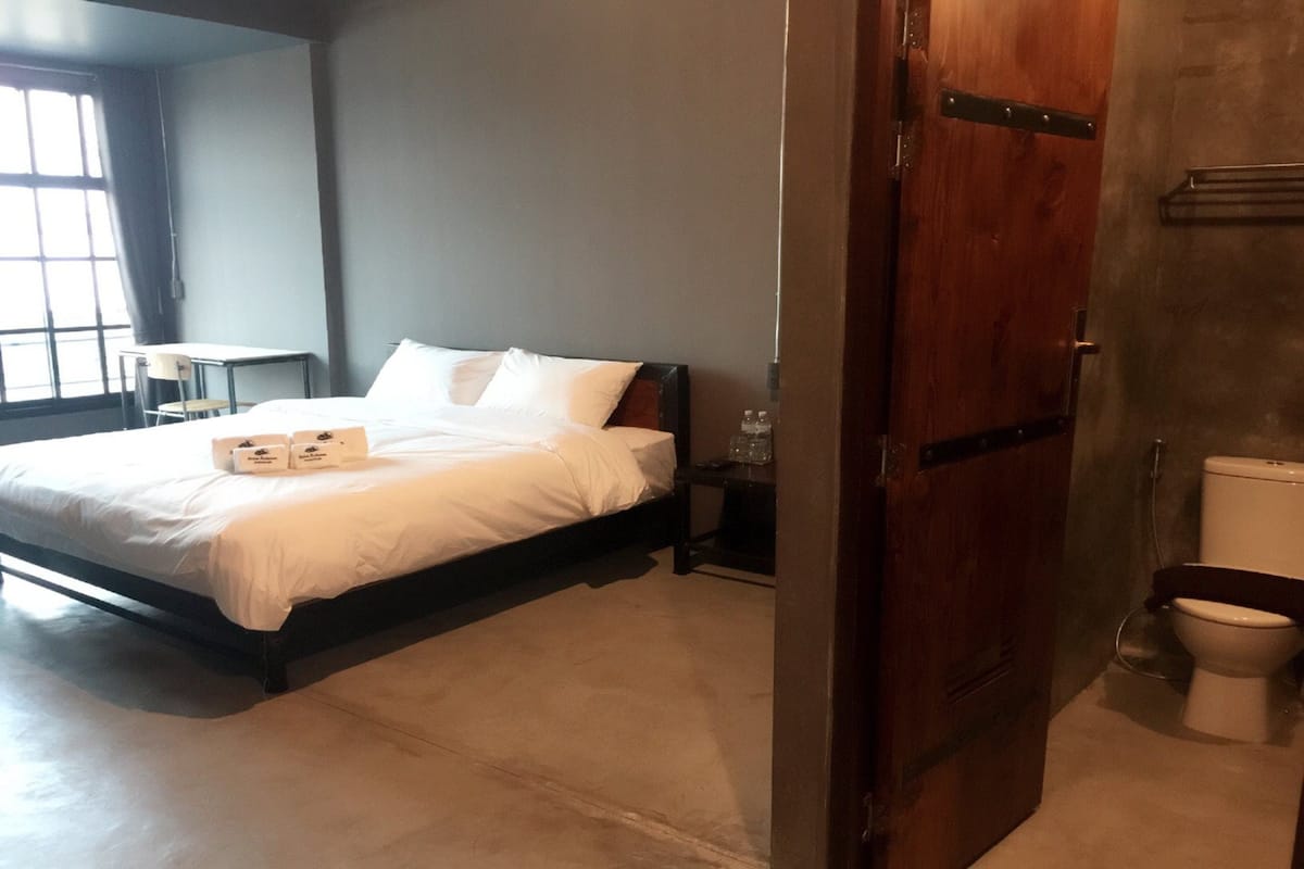 A hotel room with a bed, bedside table, and a view of a window.