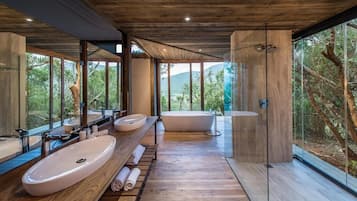 A modern bathroom with a large sink, a bathtub, and a shower area, with large windows offering a view of the outdoors.