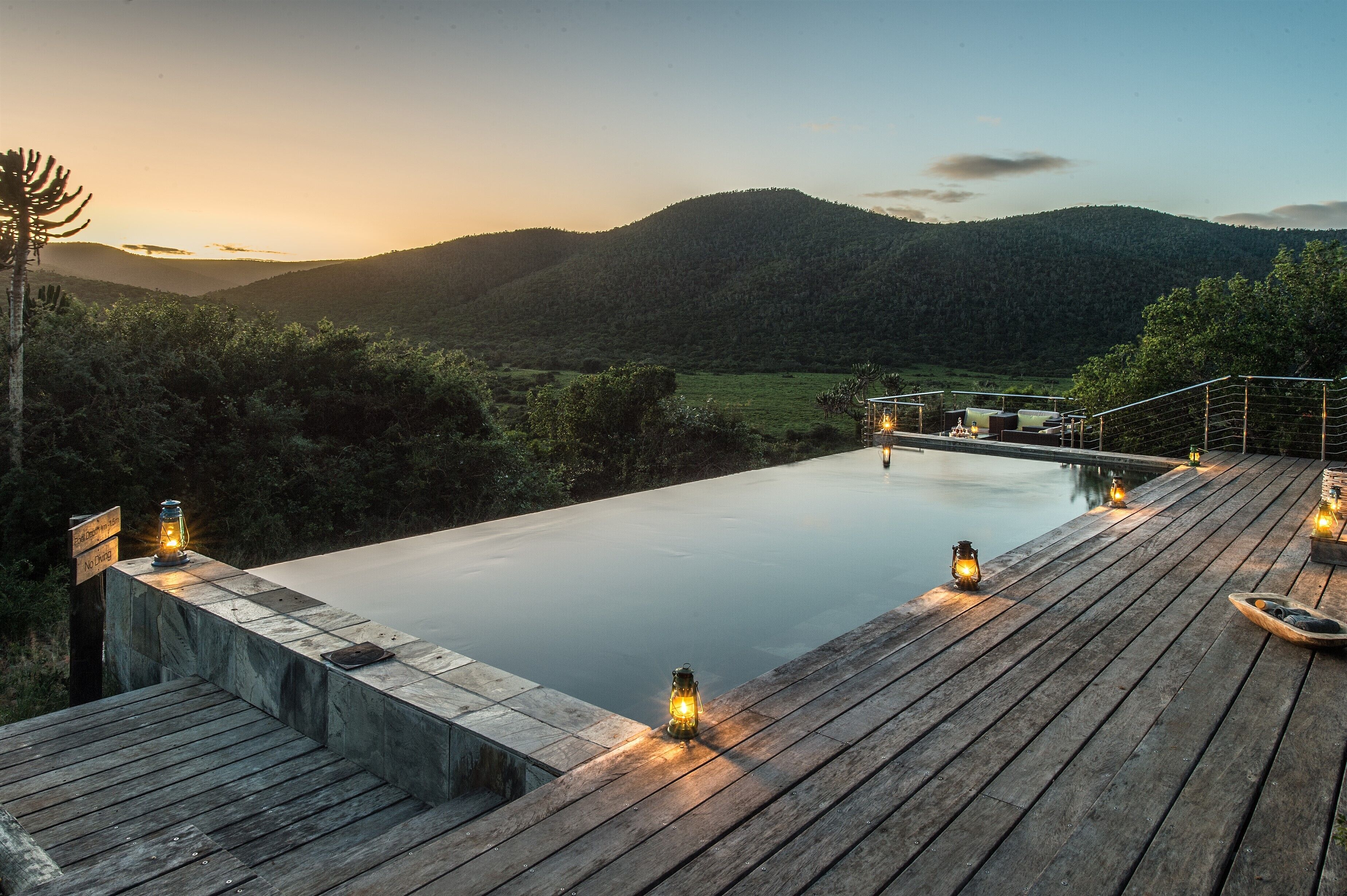 Une terrasse en bois avec une piscine, entourée d’une végétation luxuriante et de collines.