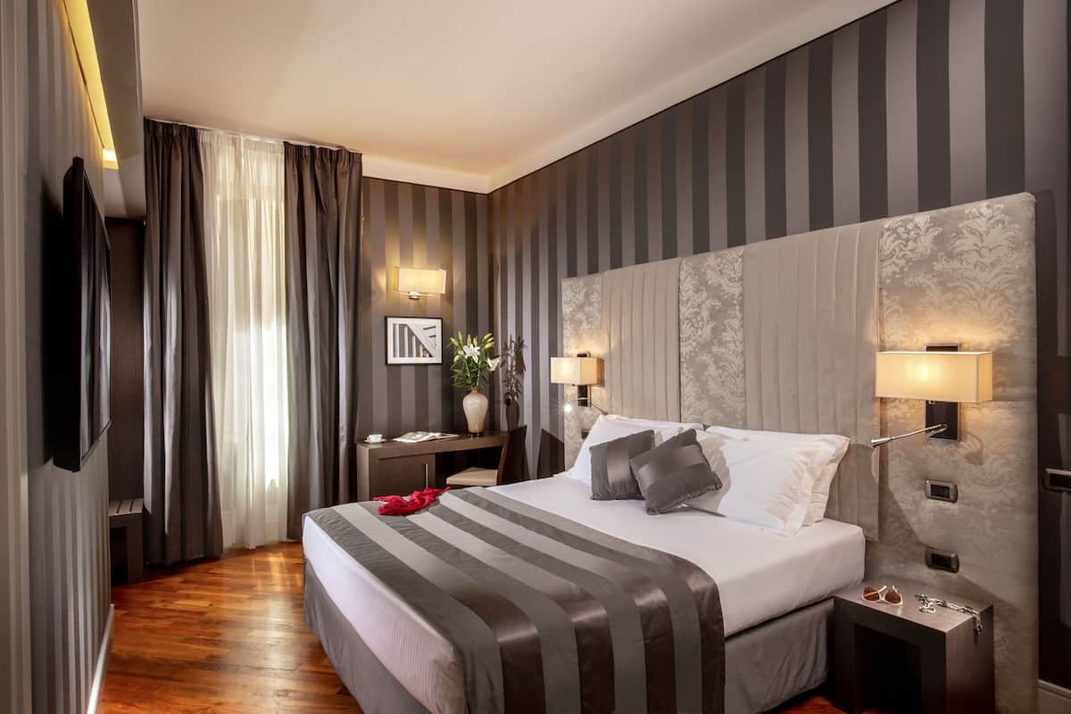 Une chambre d’hôtel moderne dotée d’un grand lit, de lampes de chevet, d’un bureau avec une chaise et d’un téléviseur fixé au mur.